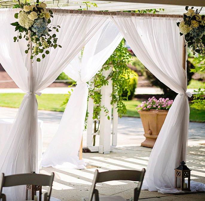 A wedding alter with a breezy canopy with white linens and flowers | Image Credit: Alyson Ridge